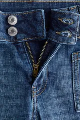 Jeans de denim azul de tiro bajo con leve elasticidad. Presentan un corte ajustado hasta el muslo y acampanado desde la rodilla. El cierre es frontal con botones en una pretina prolongada y cuenta con bolsillos delanteros de parche y bolsillos traseros.