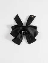 Broche para el pelo tipo clip con diseño de moño grande en tela satinada color negro. Incluye un pequeño detalle metálico dorado en uno de los extremos.