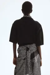 Top de punto negro con costura central delantera, mangas cortas con hombros caídos y ribete acanalado en cuello, puños y bajo.