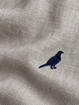 Camisa de lino color blanco, manga larga, con cuello corto clásico y bordado de un ave oscura en el pecho.
