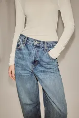 Jeans de tiro alto con corte tapered y largo al tobillo. Presenta cinco bolsillos, trabillas en la cintura, cierre frontal con cremallera y botón, y detalle de raya planchada en el delantero.