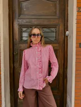 Camisa de manga larga con estampado de rayas verticales en color rojo y blanco. Presenta cuello alto con volados, cierre frontal con botones y detalles de volados en la solapa y en los puños.