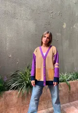 Cárdigan de lana color beige con mangas moradas, puños y ruedo en azul marino, cierre con botones marrones y bolsillos frontales de gamuza.