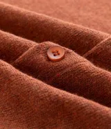 Camisa de punto jacquard color naranja, con cuello solapa, manga corta y cierre frontal con botones. Presenta detalles de rayas horizontales en contraste en el ruedo y en los puños de las mangas.