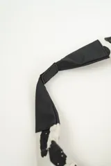 Cartera tipo hobo bag de tela color crema con estampado de manchas negras irregulares. Tiene un asa de hombro de cuero sintético negro y cierre de cremallera.