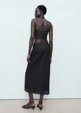 Falda midi recta de color negro, confeccionada en algodón con detalles bordados en el borde y cierre de cremallera lateral.