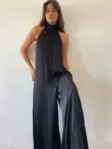 Mono largo de satén negro con escote halter y espalda descubierta. Presenta un diseño amplio y fluido con piernas anchas.