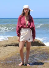 Conjunto compuesto por un pareo corto de color beige con cierre cruzado y detalle de bordado, y una bandana a juego. El pareo presenta un diseño envolvente con lazo lateral.