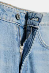Pantalón de jean celeste claro, corte cropped, tiro medio, con trabillas y cinco bolsillos. Cierre frontal con cremallera y botón metálico.