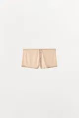 Shorts de estilo culotte confeccionados en tejido pointelle, con tiro alto y cintura elástica. Presentan una abertura frontal decorativa con botones a tono y un pequeño lazo decorativo en la cintura.