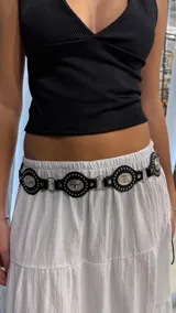 Cinturón de cuero negro con piezas metálicas plateadas unidas por argollas y decoradas con tachas y grabados de cabezas de toro.