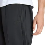 Pantalón de jogging deportivo Adidas modelo Firebird, de color negro, con cintura elástica con cordón de ajuste interno y las clásicas tiras laterales de la marca tono sobre tono. Presenta bolsillos laterales con cierre y el logo del Trifolio bordado en la pierna.