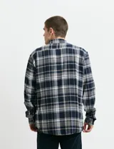 Camisa de franela a cuadros con cuello button-down, manga larga y botones de madera. Presenta dos bolsillos tipo parche en el frente con cierre de botón.