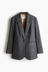Blazer de botonadura sencilla con solapas de pico, cierre de un botón frontal, hombreras, puños con botones y bolsillos delanteros ribeteados. Presenta una abertura en la parte posterior y forro interior.