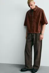 Sobrecamisa de corte relajado confeccionada en tejido efecto piel, con cuello solapa, manga corta, bolsillo plastrón en el pecho y cierre frontal con cremallera.