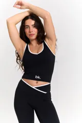 Conjunto deportivo compuesto por un top y un pantalón largo. El top es negro con ribetes blancos, escote redondo y logo 'bk.' estampado en el frente. El pantalón es negro, de corte acampanado, con cintura cruzada en V y detalle de ribete blanco.