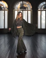 Ruana o poncho de tejido de punto negro con hilos dorados brillantes, de corte amplio y mangas largas.