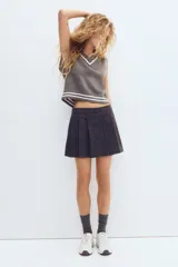 Short pollera de sarga gris oscuro con diseño tableado, rayas finas verticales y botones forrados decorativos en la parte delantera.