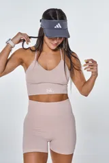 Conjunto deportivo compuesto por un top con espalda de tiras cruzadas y un short de tiro alto con efecto fruncido en la parte trasera. Ambas piezas son de color beige y presentan un diseño ajustado sin costuras.