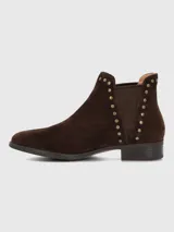 Bota corta tipo chelsea de gamuza color marrón, con detalle de tachas metálicas doradas a lo largo del elástico lateral y tacón bajo cuadrado.