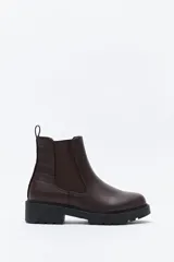 Bota tipo chelsea de caña baja con suela dentada robusta. Presenta un diseño combinado con paneles laterales elásticos, acabado liso en el frente y detalle texturizado en relieve en la parte posterior, incluyendo un tirador trasero para facilitar el calce.