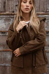Gabardina liviana color beige con capucha, cierre frontal oculto y cintura ajustable mediante cordón. Presenta bolsillos delanteros amplios y mangas largas con puños rectos.