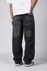 Jean de corte baggy y fit oversize, confeccionado en denim de algodón con lavado efecto gastado en color gris oscuro. Presenta costuras reforzadas en la zona de las rodillas y diseño de cinco bolsillos.