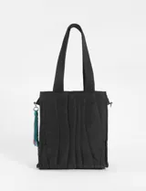 Cartera tipo shopper de color negro con diseño matelaseado de líneas onduladas. Cuenta con doble asa de hombro y un detalle de borlas colgantes en tonos vibrantes en uno de sus laterales.