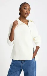 Sweater blanco de punto acanalado con cuello alto amplio y cierre de cremallera asimétrico, hombros caídos y mangas largas.