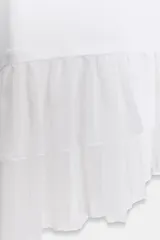 Camiseta de algodón con cuello redondo y manga corta. Presenta un bajo asimétrico confeccionado en un tejido ligero con volantes y una tira lateral decorativa con volantes.