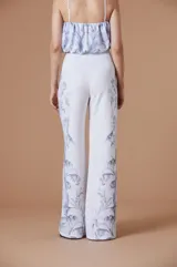 Pantalón de tiro alto con silueta amplia y corte recto, confeccionado en tela fluida color marrón con estampado botánico en tonos claros en los laterales.