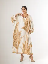 Vestido maxi túnica de corte oversized, color beige y blanco con estampa de hojas de palmera en tonos camel, mangas murciélago y bolsillos laterales.
