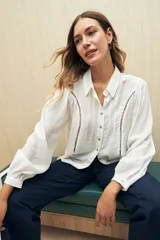 Camisa blanca de manga larga con cuello clásico y botones de nácar. Presenta detalles calados en el frente.