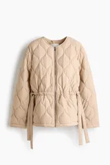 Campera acolchada de nylon beige con diseño guateado, cuello redondo y cierre frontal. Cuenta con hombros caídos, mangas largas, bolsillos laterales y cordón de ajuste en la cintura con tiras colgantes.