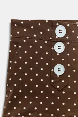 Shorts mini de tiro medio con estampado de lunares blancos sobre fondo marrón. Presenta cierre frontal decorado con botones blancos y bolsillos laterales.