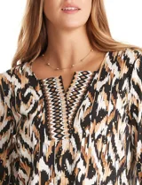 Blusa de algodón con estampado ikat en tonos blanco, negro y marrón. Presenta cuello a la base con escote en V y un patrón geométrico bordado. El estampado se realza con sutiles tachas doradas. Mangas tres cuartos con puño ancho y pequeña abertura lateral. Ruedo con tajos en los costados.