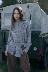 Camisa de manga larga con estampado de cuadros, cuello alto con volados y detalle de volados en el pecho. Presenta cierre frontal con botones oscuros.