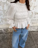 Blusa blanca con cuerpo fruncido tipo smock, cuello alto con volados y mangas largas abullonadas con puños ajustados.