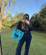 Cartera amplia de gamuza turquesa con asas de cuero marrón y aplique de caballo en pelo natural negro.