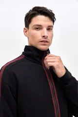 Campera de felpa con friza, de corte relajado, color negro con detalles en bordó. Presenta cuello alto, cierre frontal metálico, bolsillos laterales y cintas decorativas a contratono en las mangas.