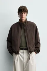 Cazadora bomber reversible de corte relaxed fit, color marrón oscuro, con cuello alto, cierre frontal de cremallera, bolsillos laterales de vivo y acabados elásticos en puños y dobladillo.