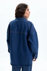 Sobrecamisa de jean color azul oscuro, con corte oversize, cuello clásico, cierre frontal con botones metálicos y dos bolsillos frontales tipo parche.