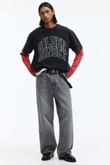 Remera boxy de algodón negro con efecto deslavado, corte oversized y mangas cortas. Presenta un estampado gráfico frontal con la inscripción "Golden Sunset" en estilo universitario.