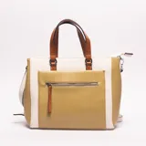 Bolso de mano tipo tote bag con diseño color block. Presenta paneles en color blanco, verde mostaza con textura de cocodrilo y beige liso. Las asas superiores son de color marrón caramelo. Incluye bolsillo exterior con cierre y correa ajustable para llevar al hombro.