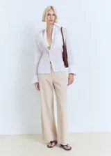 Pantalón de tiro medio color beige, de diseño recto y confeccionado en mezcla de algodón y lino. Cuenta con cuatro bolsillos, trabillas y cierre delantero con cremallera y botón.