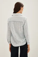 Camisa de algodón con diseño de encaje bordado, cuello clásico y frente con tablas verticales. Presenta mangas largas con puños abotonados y cierre frontal con botones.