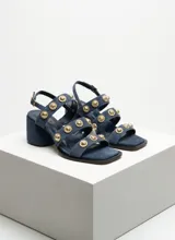Sandalias de cuero gamuzado color azul con taco cuadrado, tiras múltiples decoradas con apliques metálicos dorados circulares y tira ajustable con hebilla en el talón.