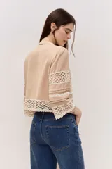 Blusa tostada con mangas tres cuartos, detalles de encaje floral calado y cierre frontal con lazos.