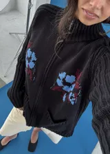 Saco de punto negro con cierre frontal y cuello alto, manga larga y bolsillos delanteros tipo ojal. Presenta diseño tejido localizado en la parte frontal en tonos celeste y bordó.