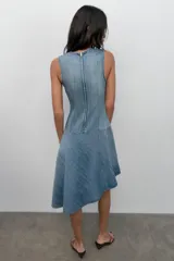 Vestido corto de denim sin mangas con cuello redondo. Presenta costuras marcadas en el cuerpo y un bajo asimétrico con vuelo.